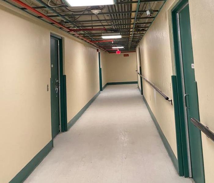School hallway is clean, cream walls outlined by green doors and floorboards sitting on a grayish white tiled floor.