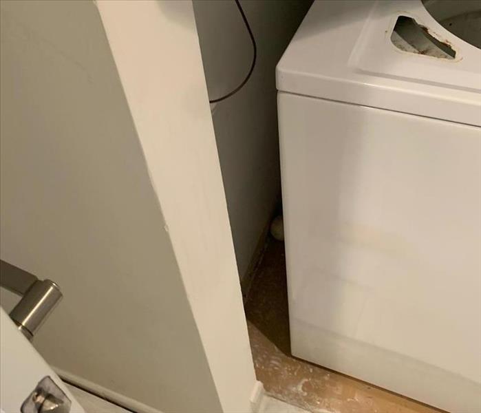 Picture is a small laundry room with a rusty washing machine on a floor stained with white dust.